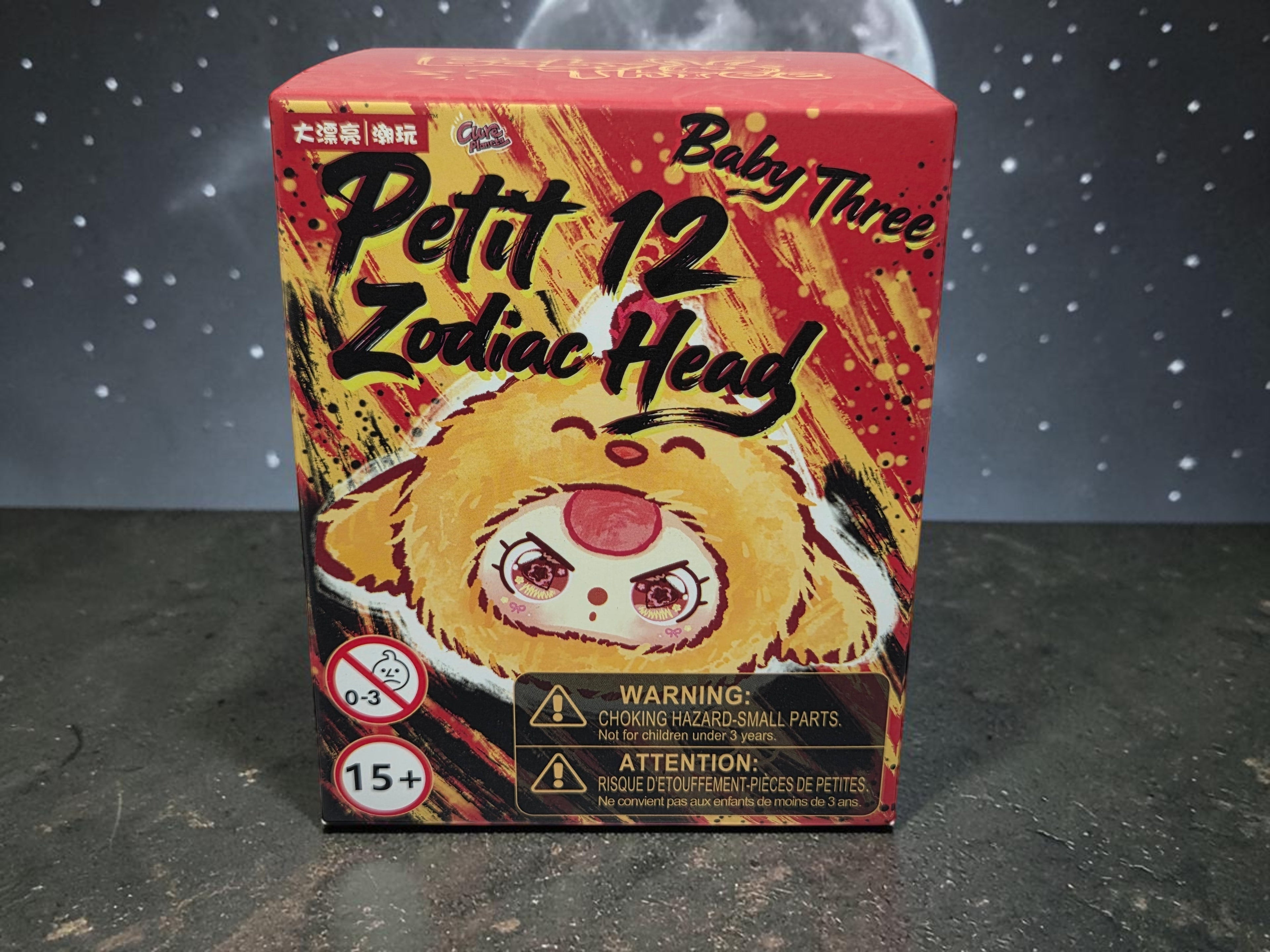 Momof2boyz Baby Three Petit 12 Zodiac Head blind box with a yellow, red, and black design featuring a cute character face. Warning labels present.