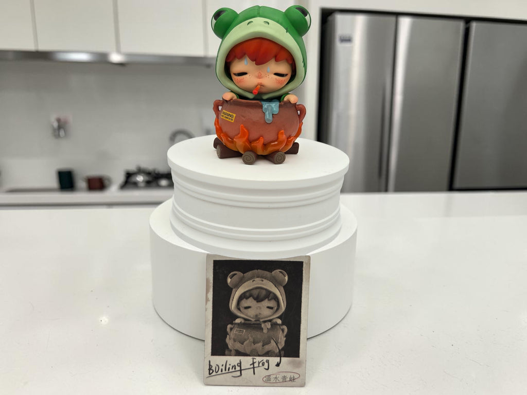Momof2boyz Hirono Tamed Wildgrass figure of a character in a frog hoodie boiling a pot over a fire.