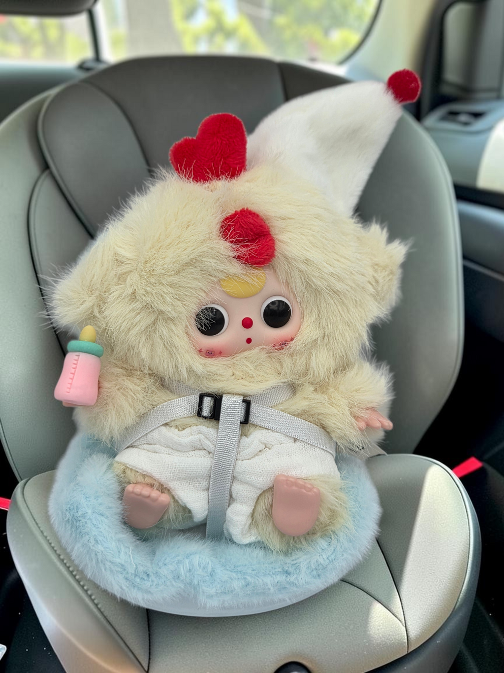 Momof2boyz Shop Baby Three BB3 plush chicken figure with a red heart, bottle, and harness in a car seat.