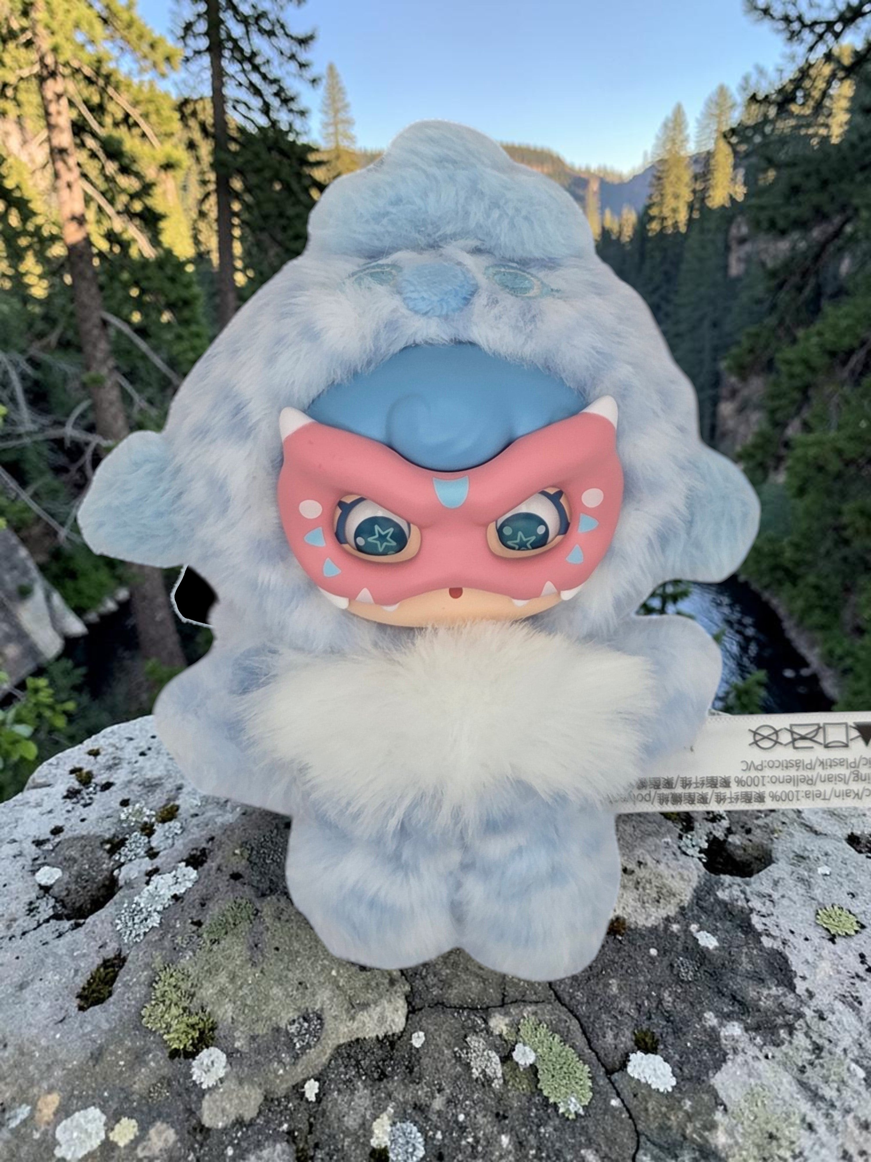 Momof2boyz Shop Mochi Little Monster plush keychain with a blue furry costume and pink character mask on a rock.