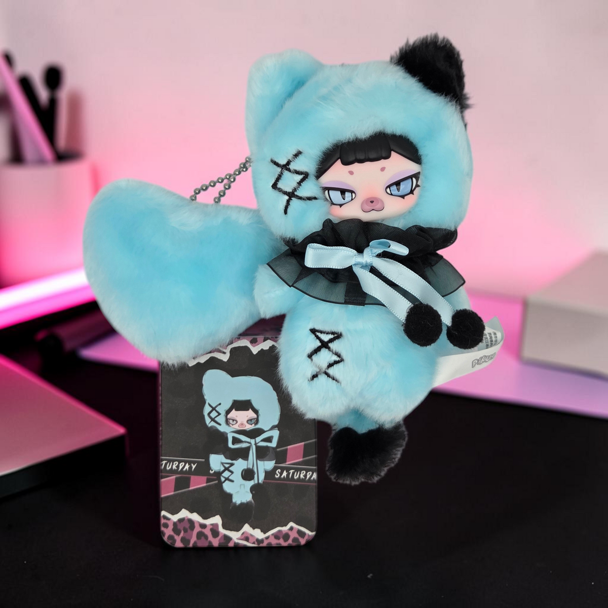 Momof2boyz Shop light blue plush keychain with black accents, heart-shaped tail, and Saturday character collector card.
