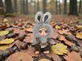 Momof2boyz Shop gray fuzzy bunny blindbox toy with brown overalls and large expressive eyes.