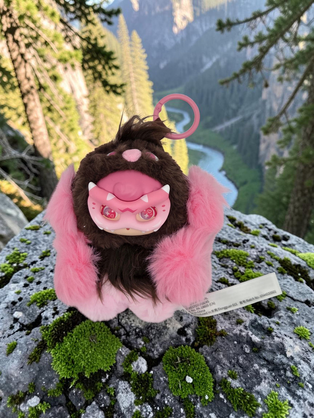 Momof2boyz Shop Mochi Little Monster plush keychain with brown and pink fur and a pink monster mask on a mossy rock