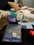 Momof2boyz Shop The Monster's 1:00 am collectible figure in green with headphones, resting on a purple cushion.