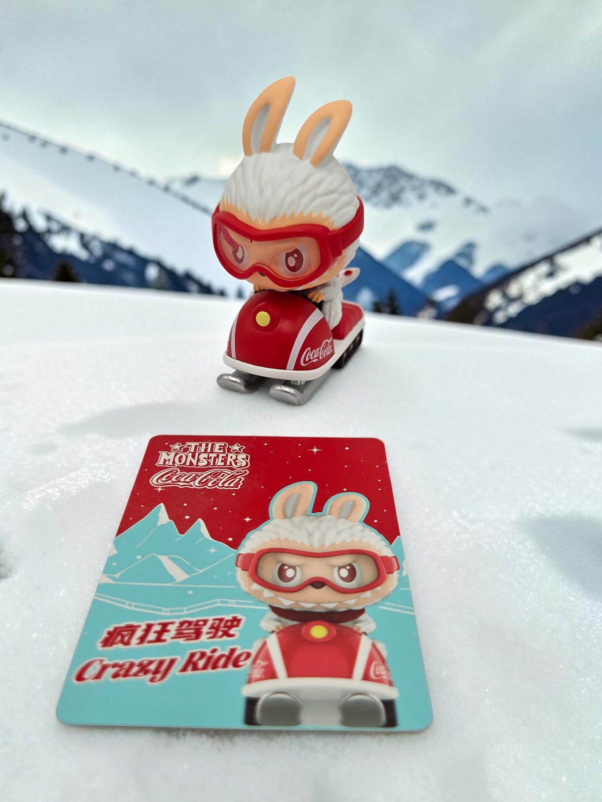 Momof2boyz Shop The Monster's Coca-Cola figure of a rabbit on a red snowmobile with a matching character card in snow.