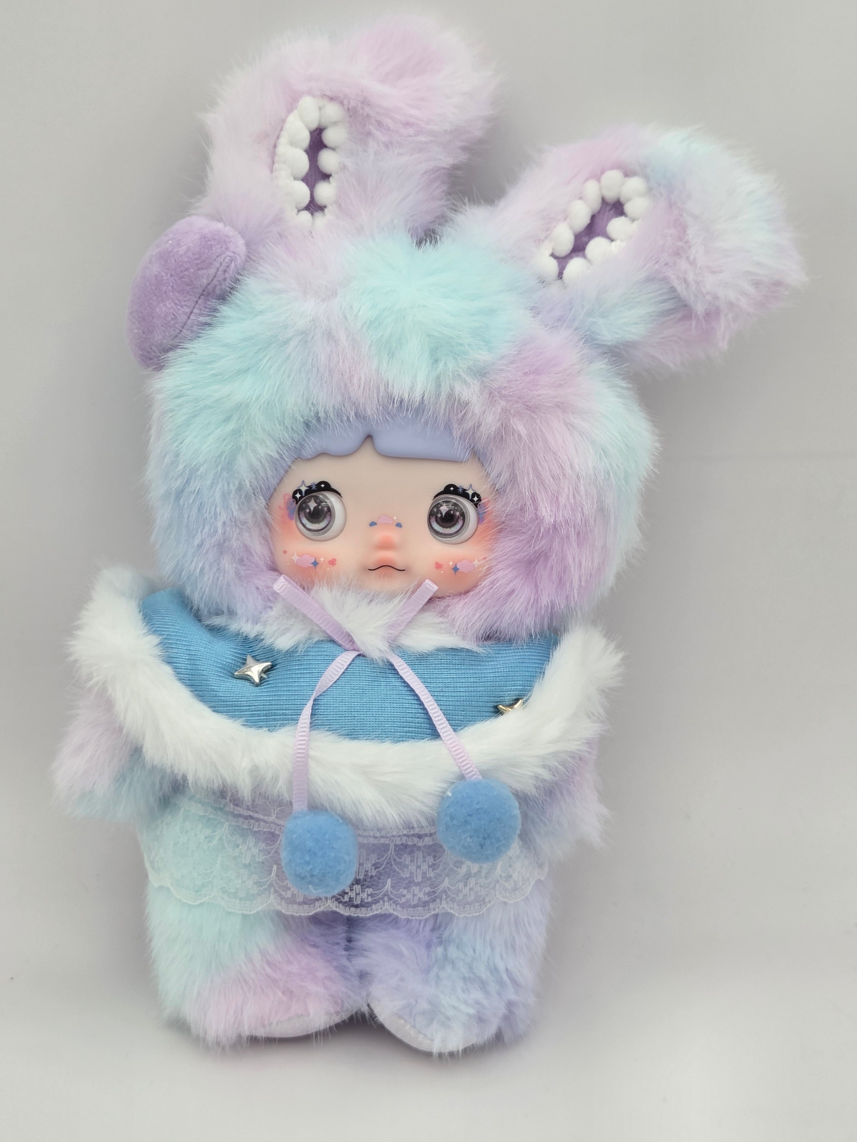Momof2boyz Shop Nommi plush doll featuring pastel blue and purple faux fur with a bunny hood and blue cape outfit.