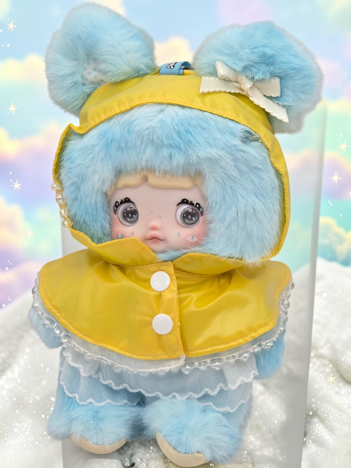 Momof2boyz Shop Nommi plush doll with blue faux fur, wearing a yellow raincoat and white lace trim
